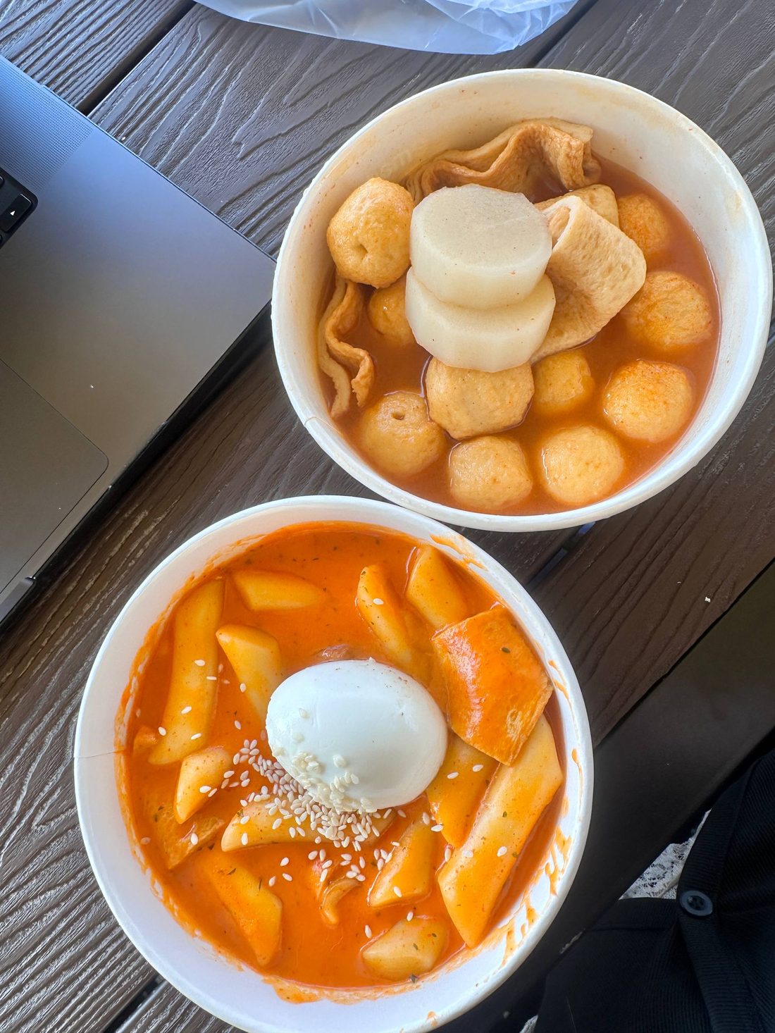 Two bowls of Korean street food: fish cake soup and rose tteokbokki topped with an egg